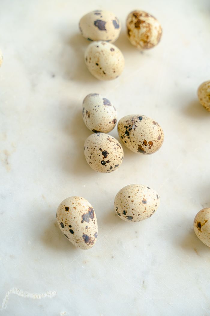 Top view of speckled quail eggs on a white marble background.