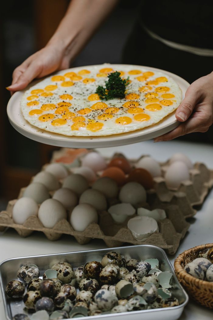 Crop unrecognizable housewife holding plate with freshly fried quail eggs above table with eggs in kitchen