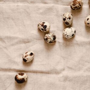 Speckled quail eggs scattered on a neutral fabric background, showcasing texture.